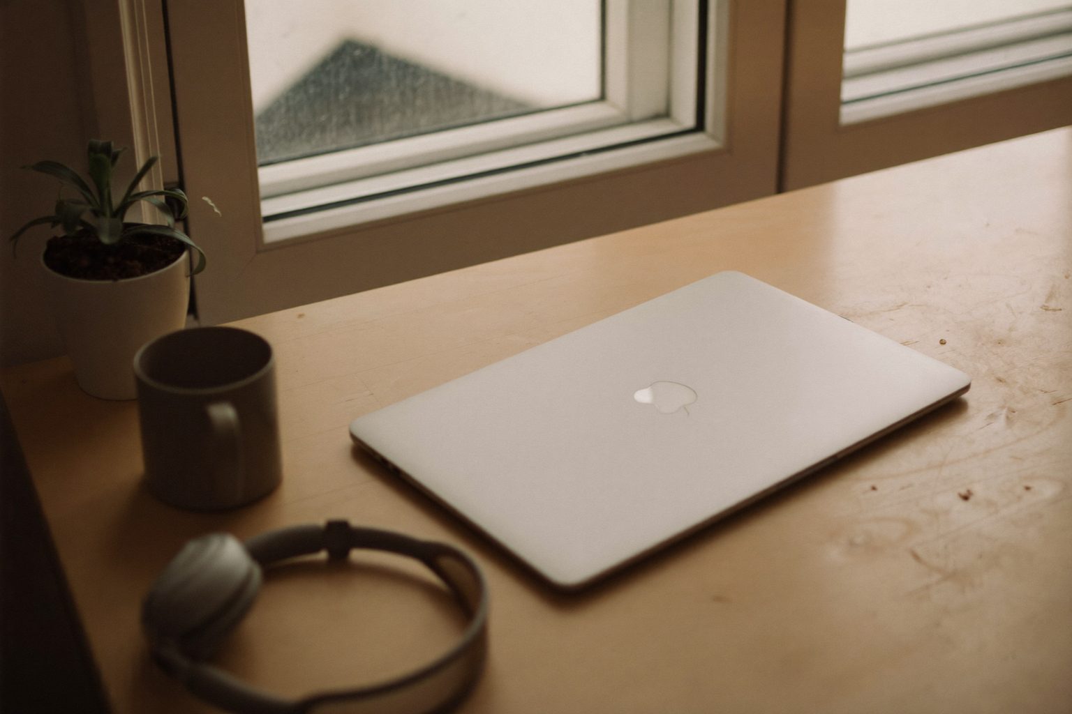 Een opgeruimd bureau bij het raam met een dichtgeklapte laptop, een koptelefoon en een kop koffie