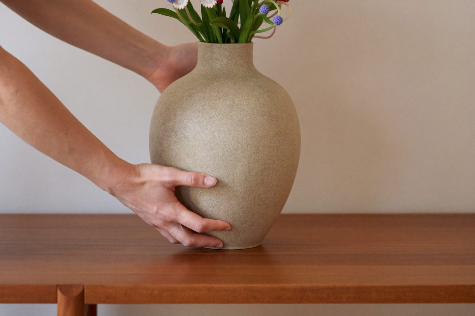 Interieurstylist schikt kussens en accessoires op een bank in een lichte, stijlvolle woonkamer