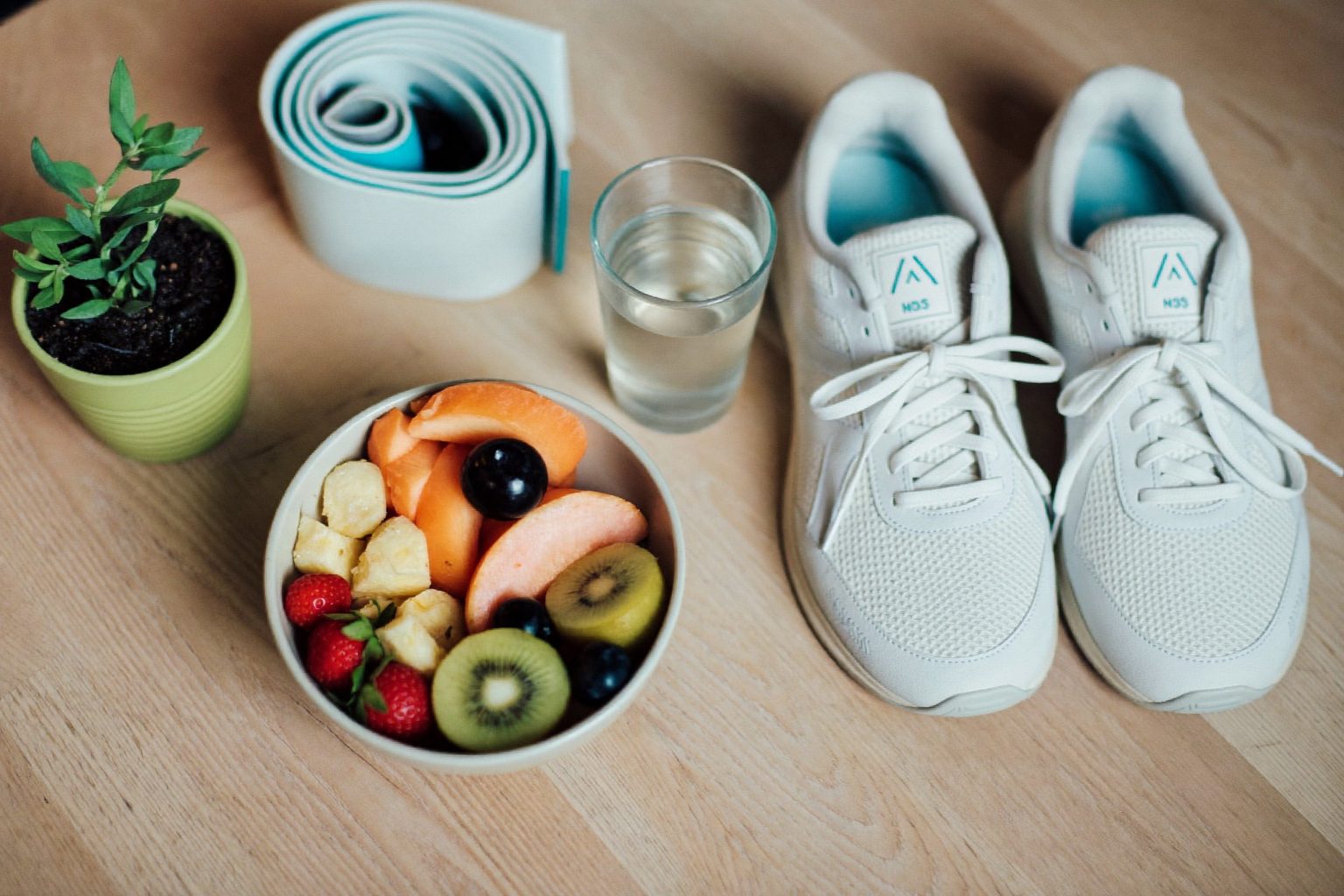 Een frisse tafel met een schaal vers fruit, een glas water, sportschoenen en een yogaband