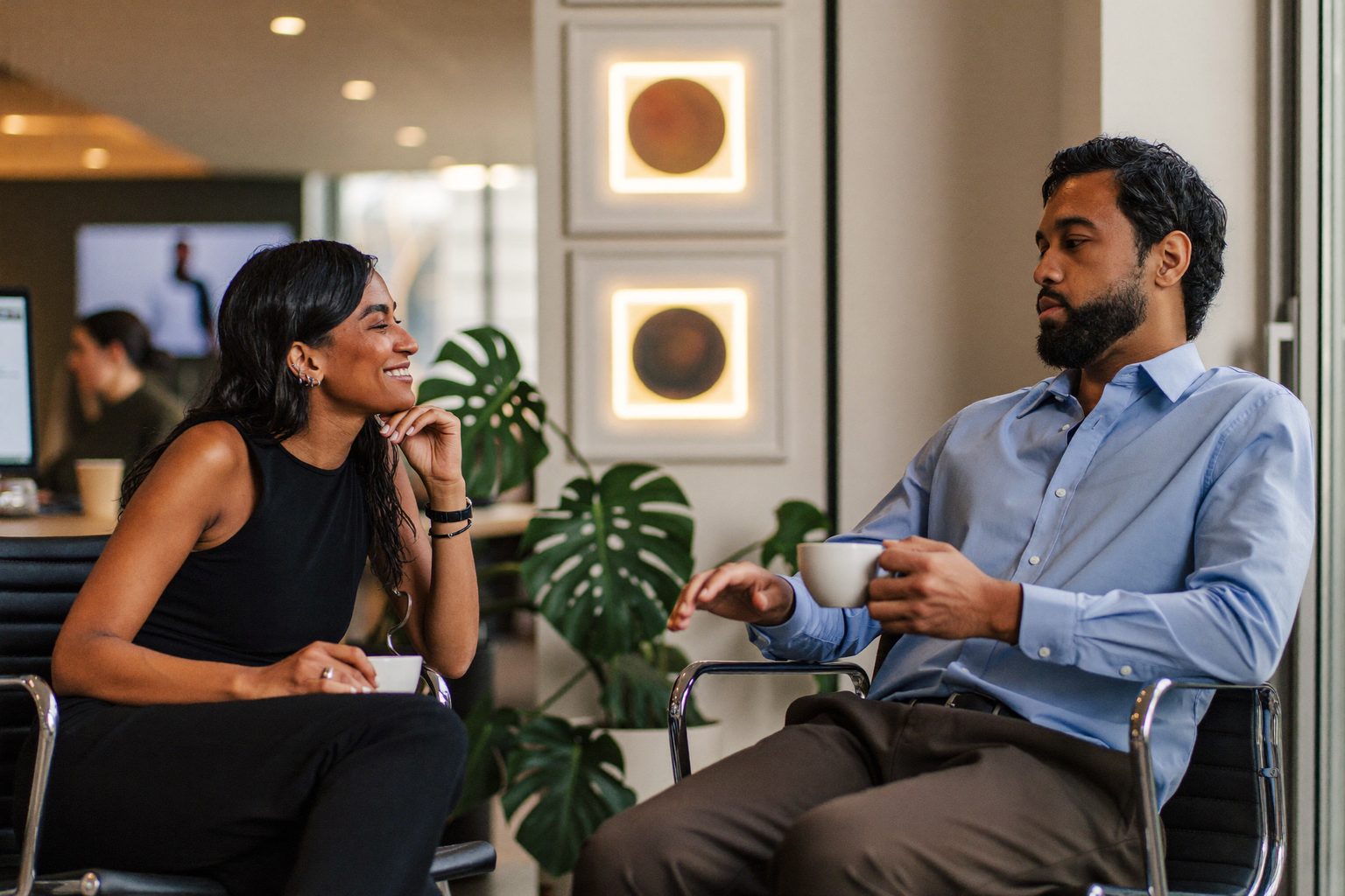 Twee collega's in gesprek met een kop koffie in een licht kantoor