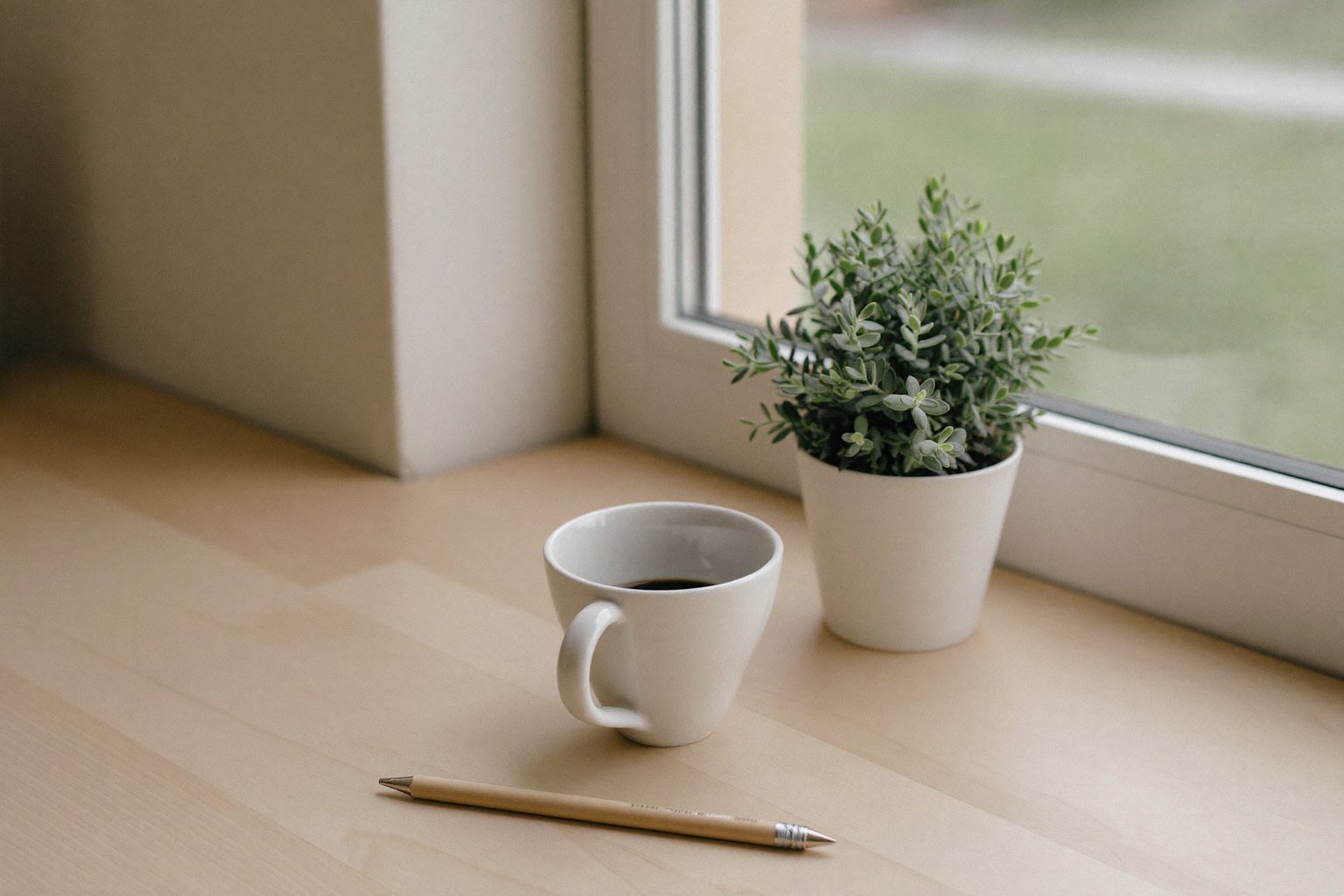 Een rustige werkplek bij het raam met een kop koffie, een plant en een potlood